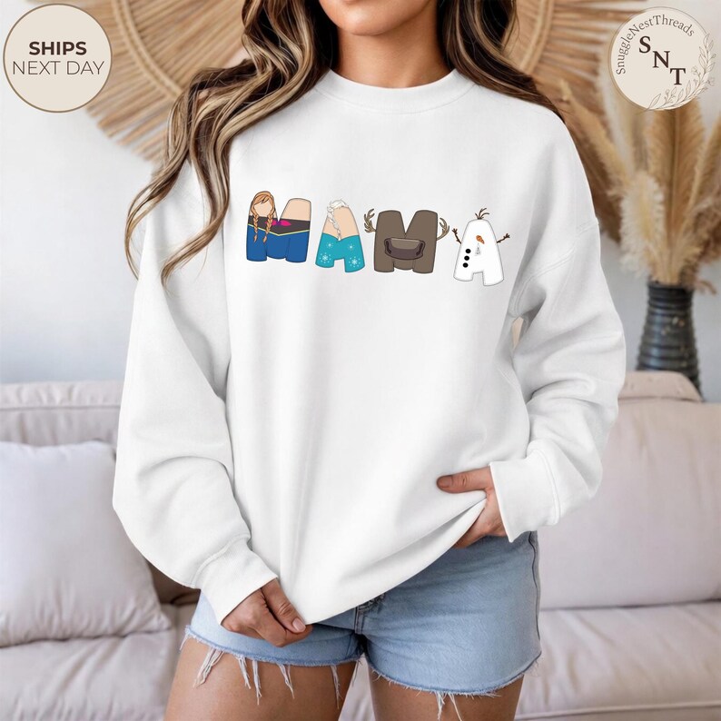 K&ouml;nnte beinhalten: Wei&szlig;es Sweatshirt mit dem Wort "MAMA" in bunten Cartoon-Buchstaben. Die Buchstaben sind so gestaltet, dass sie Figuren aus einem beliebten Zeichentrickfilm &auml;hneln. Das Sweatshirt hat einen Rundhalsausschnitt und lange &Auml;rmel.