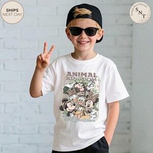 Pu&ograve; includere: T-shirt bianca con una grafica dei personaggi Disney di Animal Kingdom, tra cui Topolino e Minnie, Paperino e Paperina, e Pippo. La maglietta presenta anche la scritta "Walt Disney World".