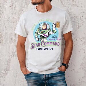 Puede incluir: Camiseta blanca con una ilustraci&oacute;n de dibujos animados de Buzz Lightyear sosteniendo una jarra de cerveza. El dise&ntilde;o incluye el texto "Buzz Lite Beer" y "Star Command Brewery" en una fuente circular y estilizada. La camiseta tambi&eacute;n tiene el texto "Best Quality Since 1995".
