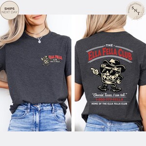Puede incluir: Camiseta gris oscuro con el texto "ELLA FELLA CLUB" y una imagen de dibujos animados de un vaso de whisky con sombrero de vaquero y gafas de sol. La parte trasera de la camiseta tiene el mismo gr&aacute;fico y la frase "Choosin' Texas, I can tell."