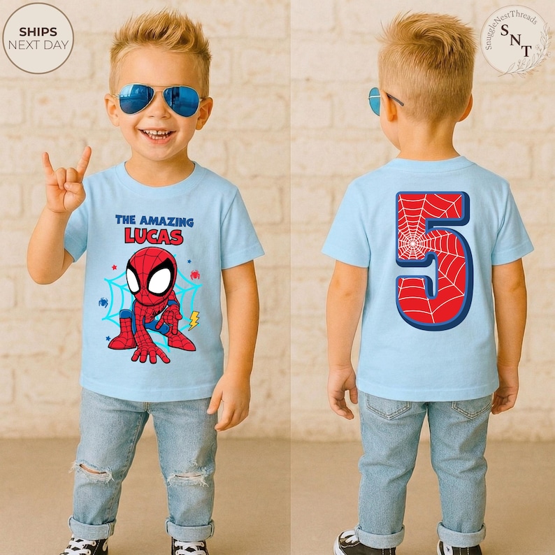 Puede incluir: Camiseta azul claro con tem&aacute;tica de Spider-Man con el texto "THE AMAZING LUCAS" y un gr&aacute;fico de Spider-Man. La parte posterior de la camiseta presenta el n&uacute;mero 5 con un dise&ntilde;o de telara&ntilde;a. El ni&ntilde;o lleva vaqueros azules.