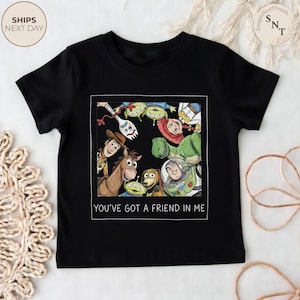 May include: Black t-shirt featuring a colorful graphic of characters from the movie Toy Story. The image includes Woody, Buzz Lightyear, and other characters, with the text "YOU'VE GOT A FRIEND IN ME" below the graphic.
