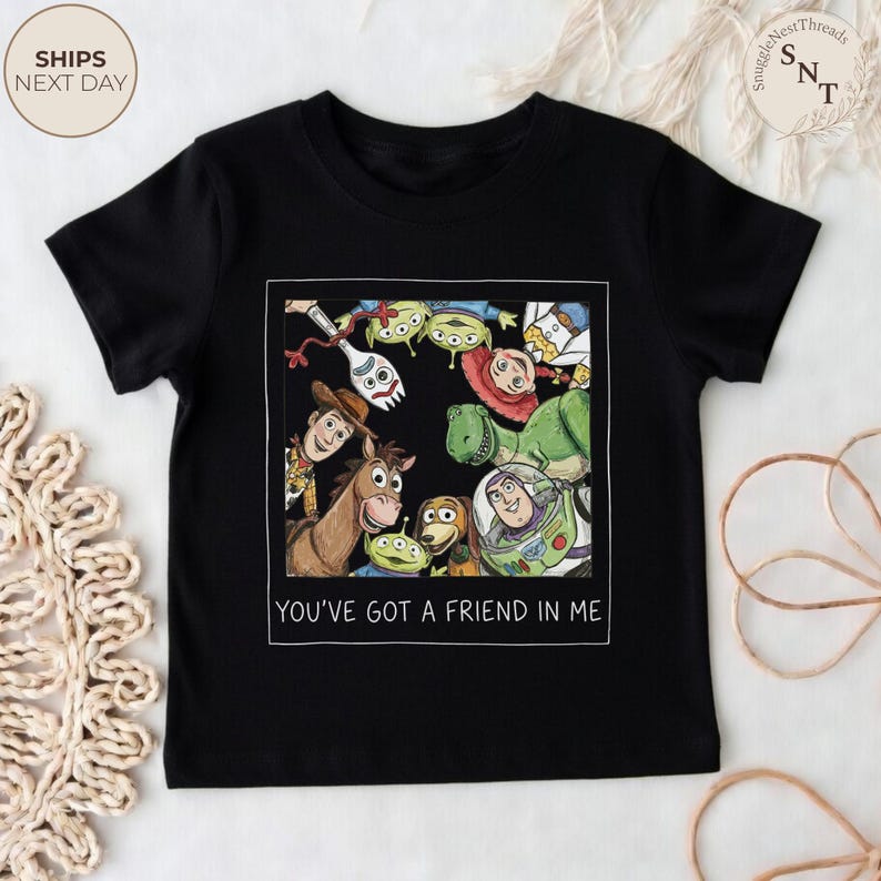 May include: Black t-shirt featuring a colorful graphic of characters from the movie Toy Story. The image includes Woody, Buzz Lightyear, and other characters, with the text "YOU'VE GOT A FRIEND IN ME" below the graphic.