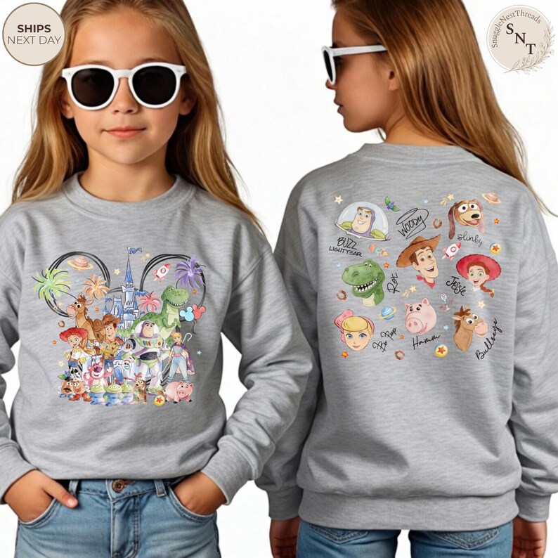 Puede incluir: Una sudadera gris jaspeado de cuello redondo con un gr&aacute;fico colorido de personajes de Toy Story en la parte delantera y un estampado trasero que muestra varias caras, nombres y firmas de personajes como Buzz Lightyear, Woody, Jessie y Rex.