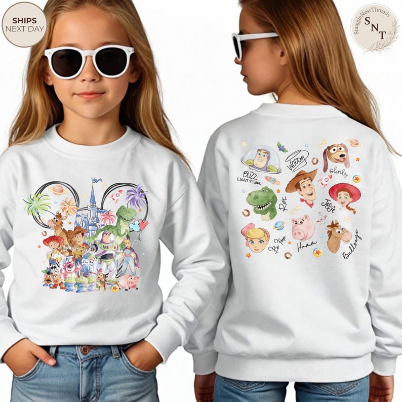 Puede incluir: Una sudadera blanca de manga larga con un gr&aacute;fico colorido de personajes de Toy Story y un castillo en la parte delantera, y una colecci&oacute;n de rostros de personajes con sus nombres escritos en cursiva en la parte trasera.