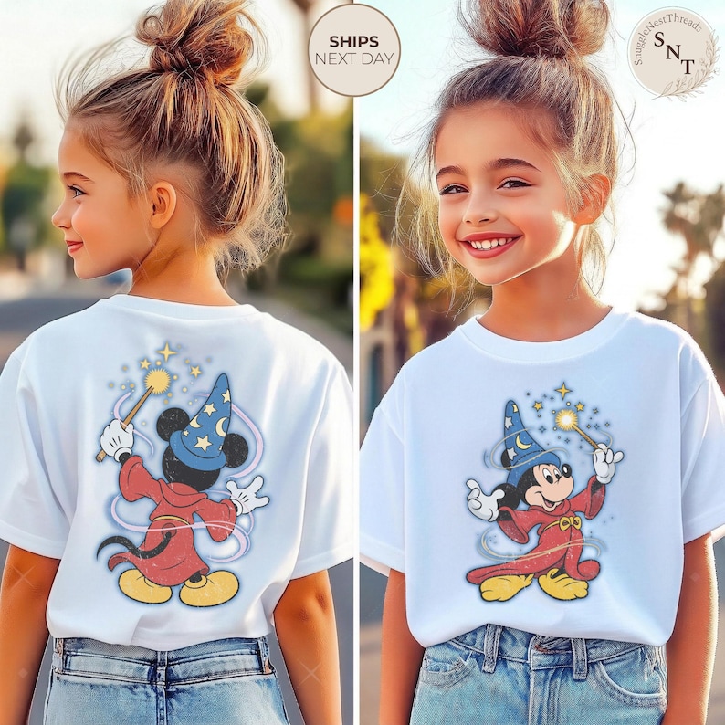 Op de afbeelding: Wit T-shirt met een afbeelding van Mickey Mouse als tovenaar, met een toverstaf met sterren. Het ontwerp is rood, blauw en geel. Het T-shirt wordt gedragen door een jong persoon met een blauwe jeans.