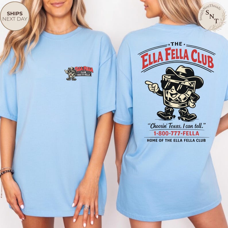 Puede incluir: Camisetas de color azul claro con el texto "The Ella Fella Club" en rojo y negro. La parte delantera de la camiseta tiene un peque&ntilde;o logotipo, y la parte trasera presenta una imagen de dibujos animados de un vaso de whisky con sombrero de vaquero y botas.