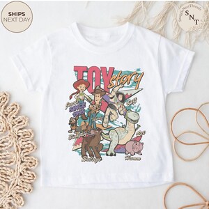 Puede incluir: Una camiseta blanca de manga corta con un estampado gr&aacute;fico colorido de los personajes de Toy Story, incluyendo a Jessie, Woody, Buzz Lightyear, Slinky Dog, Bullseye, Rex y Hamm. El dise&ntilde;o incluye el texto Toy Story y los nombres.