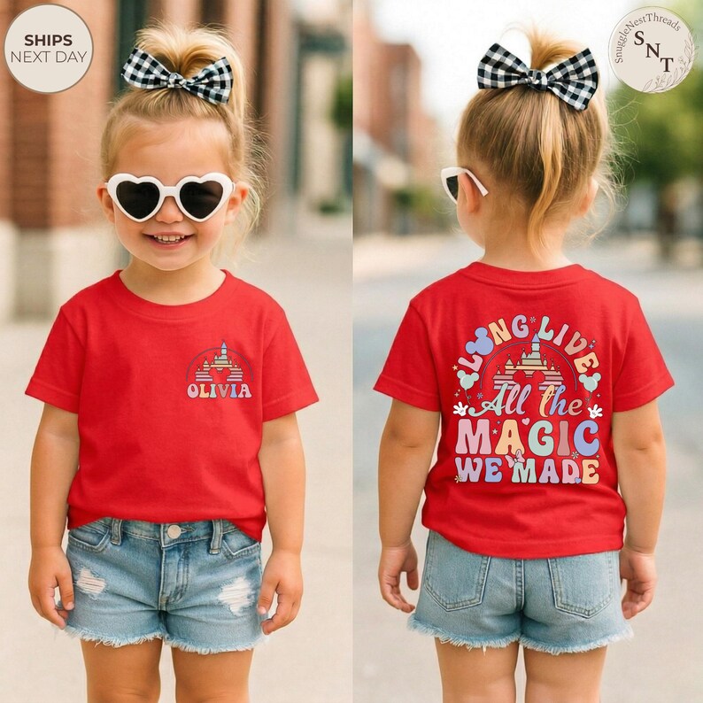 May include: A red t-shirt with the text "OLIVIA" and a castle graphic on the front. The back of the shirt features the text "LONG LIVE All The MAGIC WE MADE". The child is wearing denim shorts and sunglasses.