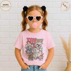 Puede incluir: Una camiseta de manga corta de color rosa claro con un estampado gr&aacute;fico colorido de los personajes de Toy Story, incluyendo a Woody, Buzz Lightyear, Jessie, Rex, Slinky Dog, Bullseye y Hamm, con el texto Toy Story y los nombres.