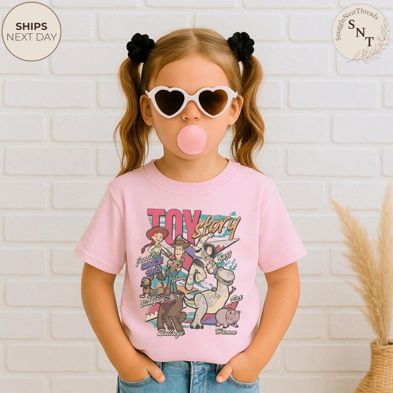 Puede incluir: Una camiseta de manga corta de color rosa claro con un estampado gr&aacute;fico colorido de los personajes de Toy Story, incluyendo a Woody, Buzz Lightyear, Jessie, Rex, Slinky Dog, Bullseye y Hamm, con el texto Toy Story y los nombres.