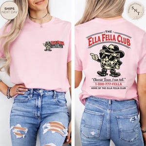 Puede incluir: Camiseta rosa claro con el logo "The Ella Fella Club" en la parte delantera y trasera. La parte delantera tiene un peque&ntilde;o gr&aacute;fico y texto, mientras que la parte trasera muestra un dise&ntilde;o m&aacute;s grande con un personaje de dibujos animados y texto.