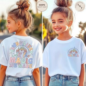 May include: White t-shirt with a colorful castle graphic and the name "Olivia" printed on the front. The back of the shirt features the text "Long Live All the Magic We Made" in pastel colors. The shirt is worn by a young girl.