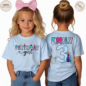 K&ouml;nnte beinhalten: Zwei junge M&auml;dchen tragen hellblaue T-Shirts mit Geburtstagsmotiven. Auf der Vorderseite des Shirts steht "Birthday girl" mit Schneeflocken-Akzenten. Auf der R&uuml;ckseite des Shirts stehen der Name "Emily" und die Zahl "3" mit Frozen-Figuren.