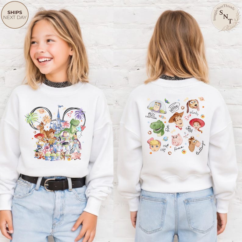 Puede incluir: Una sudadera blanca de manga larga con un gr&aacute;fico frontal de personajes de Toy Story dispuestos en forma de orejas de Mickey Mouse con un castillo, y un gr&aacute;fico trasero que muestra caras de personajes como Buzz, Woody y Jessie con nombres.