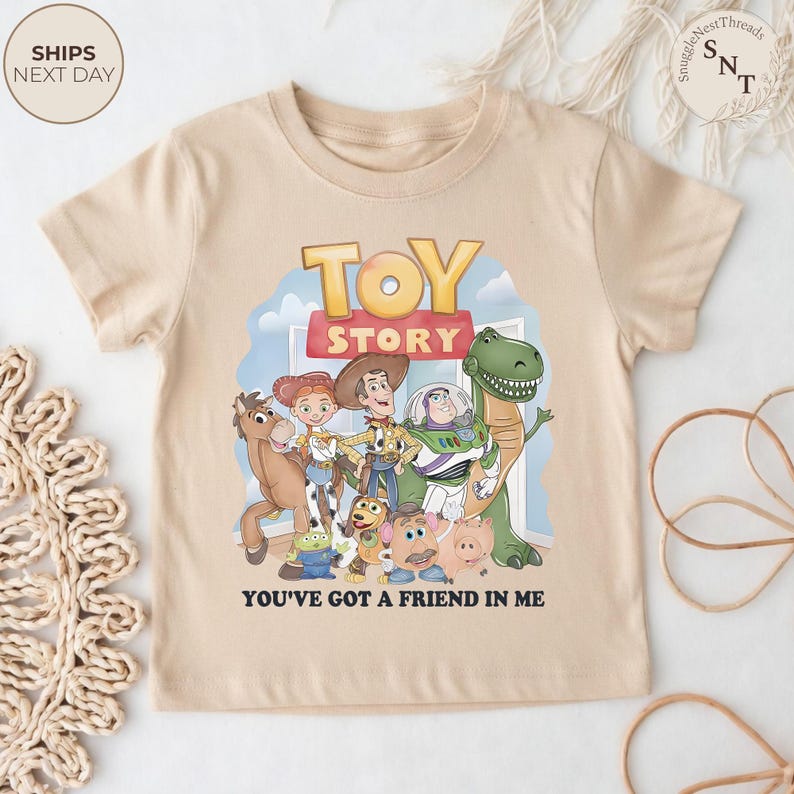K&ouml;nnte beinhalten: Beiges kurz&auml;rmeliges T-Shirt mit dem Schriftzug "TOY STORY" in einem farbenfrohen Design, mit Zeichentrickfiguren aus dem Film. Der Satz "YOU'VE GOT A FRIEND IN ME" ist darunter gedruckt. Das T-Shirt hat einen Rundhalsausschnitt.