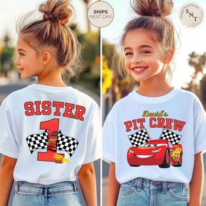 May include: White t-shirts with racing-themed graphics. One shirt says "SISTER 1" with checkered flags and a race car. The other says "David's PIT CREW" with a red race car and checkered flags. Both shirts are worn by a young person.