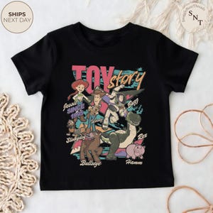 Puede incluir: Una camiseta negra de manga corta con un estampado gr&aacute;fico colorido de los personajes de Toy Story, incluyendo a Jessie, Woody, Buzz Lightyear, Slinky Dog, Bullseye, Rex y Hamm, con el texto Toy Story, Jessie Since 1995 y los nombres.