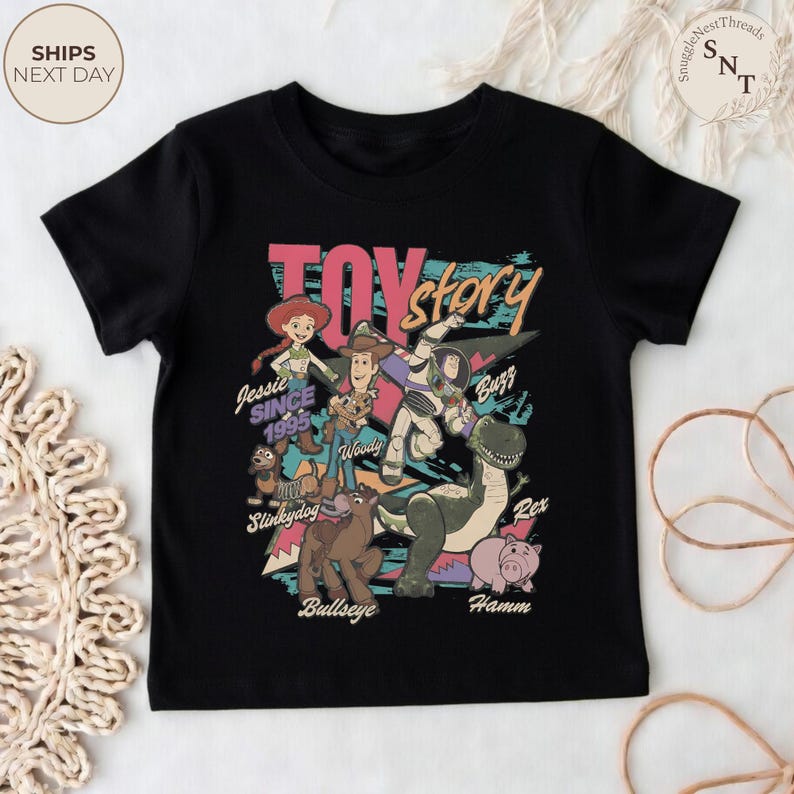 Puede incluir: Una camiseta negra de manga corta con un estampado gr&aacute;fico colorido de los personajes de Toy Story, incluyendo a Jessie, Woody, Buzz Lightyear, Slinky Dog, Bullseye, Rex y Hamm, con el texto Toy Story, Jessie Since 1995 y los nombres.