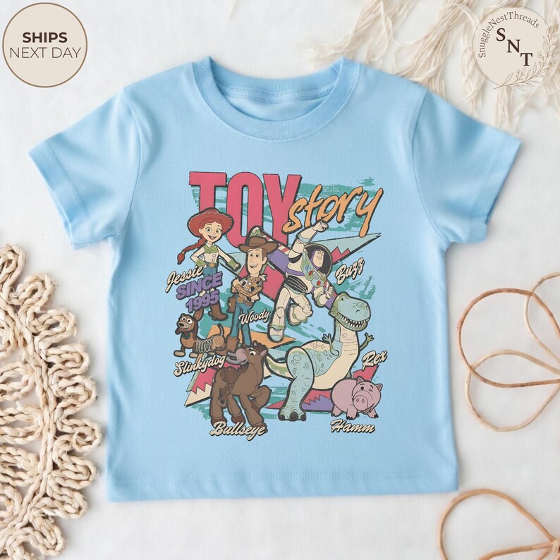 Puede incluir: Una camiseta de manga corta de color azul claro con un estampado gr&aacute;fico de los personajes de Toy Story, incluyendo a Woody, Buzz Lightyear, Jessie, Slinky Dog, Bullseye, Rex y Hamm. El texto dice Toy Story, Jessie Since 1995, Woody, Buzz, Slinky Dog, Bullseye, Rex y Hamm.