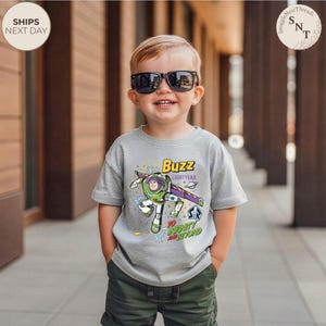 Puede incluir: Un ni&ntilde;o peque&ntilde;o con una camiseta gris con un dise&ntilde;o de Buzz Lightyear y el texto "Buzz Lightyear" y "To Infinity and Beyond". El ni&ntilde;o tambi&eacute;n lleva gafas de sol y pantalones cortos verdes. El fondo es borroso.