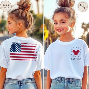 May include: White t-shirts with patriotic designs. One shirt features a distressed American flag on the back. The other has a Mickey Mouse head with stars and the name "Scarlet". Both shirts are worn by a young person.