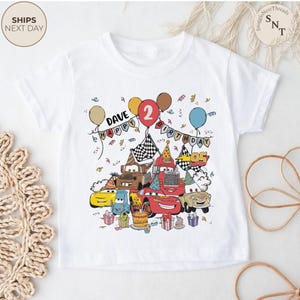 Puede incluir: Camiseta blanca con un estampado colorido de coches de dibujos animados, globos y confeti. El dise&ntilde;o incluye el texto "DAVE HAPPY BIRTHDAY 2". Los coches son de varios colores, con tem&aacute;tica de cumplea&ntilde;os.