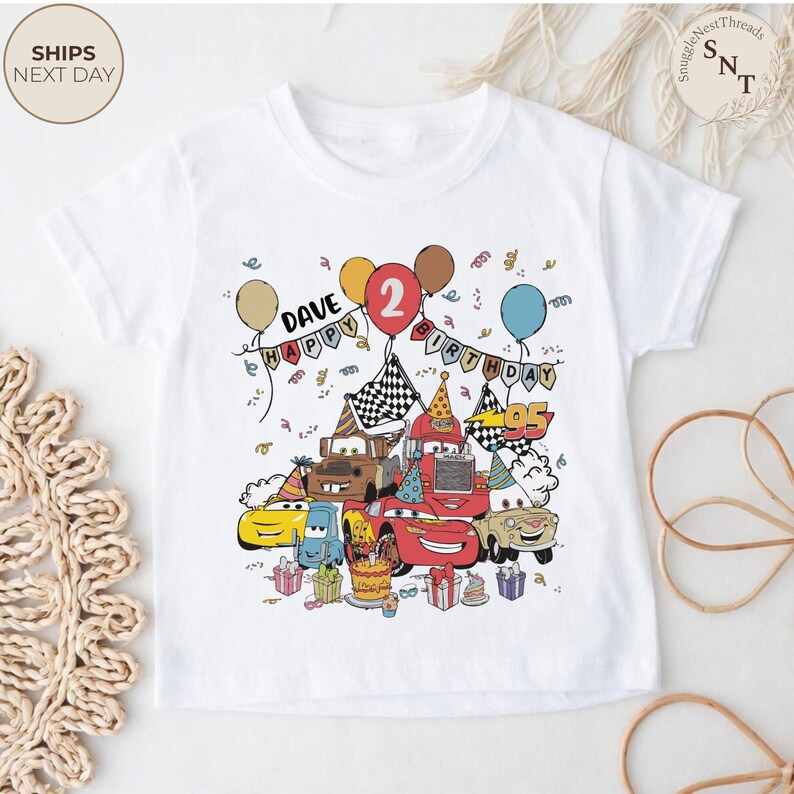 Puede incluir: Camiseta blanca con un estampado colorido de coches de dibujos animados, globos y confeti. El dise&ntilde;o incluye el texto "DAVE HAPPY BIRTHDAY 2". Los coches son de varios colores, con tem&aacute;tica de cumplea&ntilde;os.