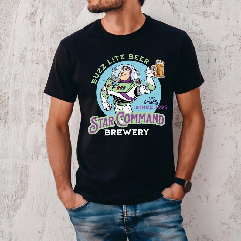 Puede incluir: Camiseta negra con una ilustraci&oacute;n de dibujos animados de Buzz Lightyear sosteniendo una jarra de cerveza. El dise&ntilde;o incluye el texto "Buzz Lite Beer" y "Star Command Brewery, Best Quality Since 1995".