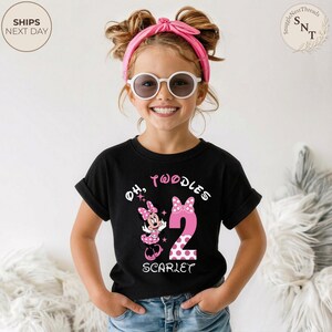 Puede incluir: Una camiseta negra con un dise&ntilde;o de Minnie Mouse rosa y el texto "Oh, Twoodles 2 Scarlet". El n&uacute;mero 2 es rosa con lunares blancos. La ni&ntilde;a lleva gafas de sol y una diadema rosa.