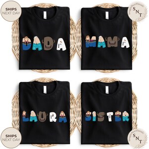 K&ouml;nnte beinhalten: Vier schwarze T-Shirts mit wei&szlig;em Text und Charakterdesigns, die "DADA", "MAMA", "LAURA" und "SISTER" buchstabieren. Die Shirts werden auf einem gewebten Hintergrund pr&auml;sentiert. Der Text "SHIPS NEXT DAY" ist sichtbar.