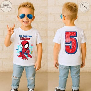 Puede incluir: Una camiseta blanca con un dise&ntilde;o de Spider-Man y el texto "THE AMAZING LUCAS" en la parte delantera. La parte trasera de la camiseta muestra un gran n&uacute;mero 5 con un dise&ntilde;o de telara&ntilde;a. El ni&ntilde;o lleva vaqueros azules y gafas de sol.