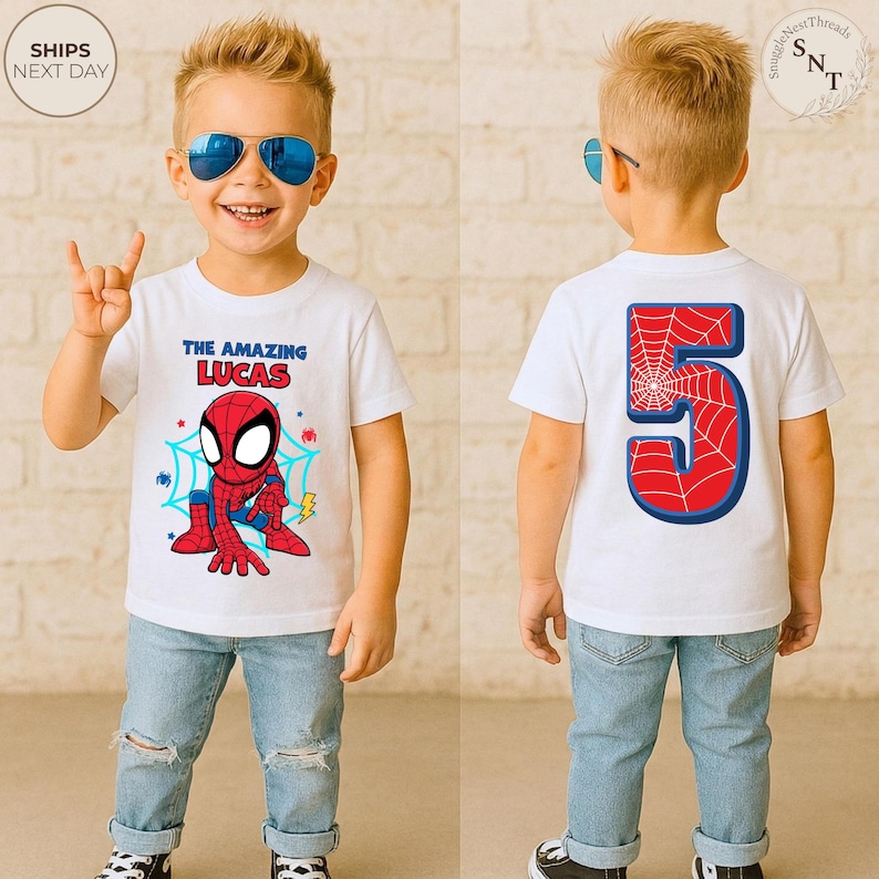Puede incluir: Una camiseta blanca con un dise&ntilde;o de Spider-Man y el texto "THE AMAZING LUCAS" en la parte delantera. La parte trasera de la camiseta muestra un gran n&uacute;mero 5 con un dise&ntilde;o de telara&ntilde;a. El ni&ntilde;o lleva vaqueros azules y gafas de sol.