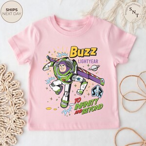 Puede incluir: Camiseta rosa claro con un dise&ntilde;o de Buzz Lightyear. El dise&ntilde;o incluye el texto "Buzz Lightyear" y "To Infinity and Beyond". Buzz aparece con su traje espacial verde, blanco y morado. Es una prenda infantil.