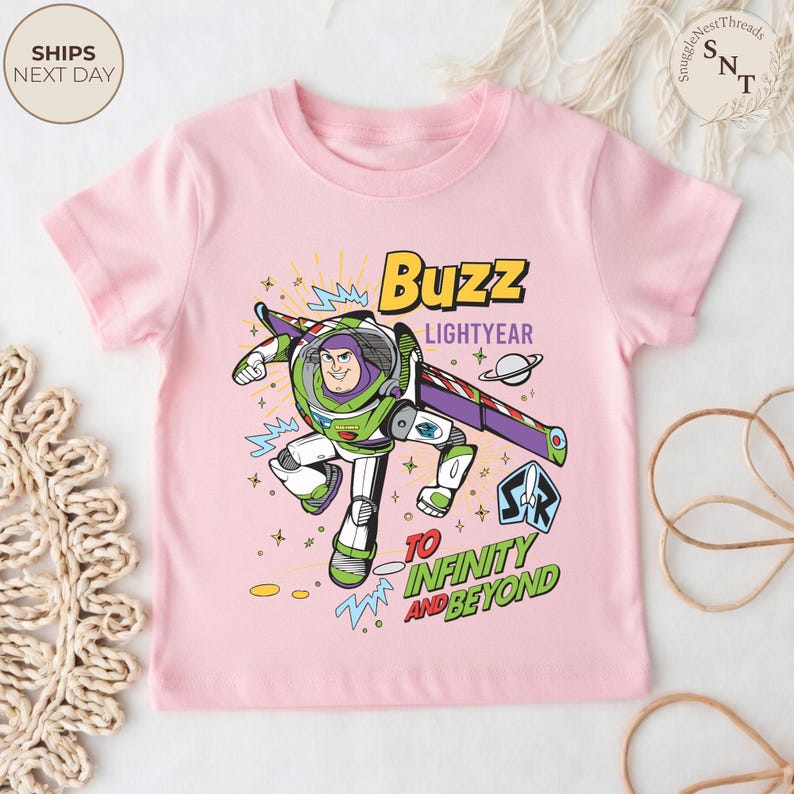 Puede incluir: Camiseta rosa claro con un dise&ntilde;o de Buzz Lightyear. El dise&ntilde;o incluye el texto "Buzz Lightyear" y "To Infinity and Beyond". Buzz aparece con su traje espacial verde, blanco y morado. Es una prenda infantil.