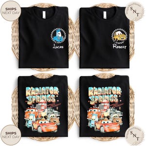 May include: Four black t-shirts with different designs. Two shirts feature cartoon car graphics with names "Lucas" and "Robert". The other two shirts display a colorful "Radiator Springs" design with various car characters. All shirts are on a woven background.