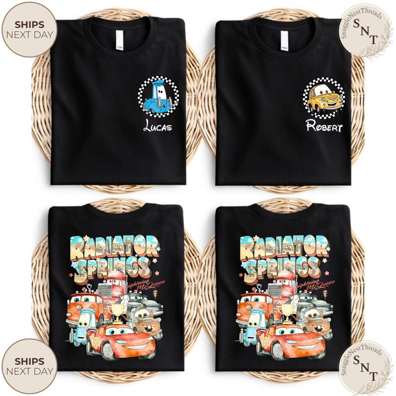 May include: Four black t-shirts with different designs. Two shirts feature cartoon car graphics with names "Lucas" and "Robert". The other two shirts display a colorful "Radiator Springs" design with various car characters. All shirts are on a woven background.