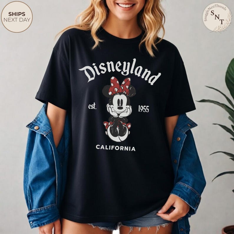 Pu&ograve; includere: T-shirt nero con grafica di Minnie Mouse, fiocco a pois rossi e la scritta "Disneyland est. 1955 California". Un design classico per i fan Disney.