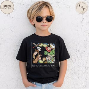 May include: Black t-shirt featuring a colorful graphic of characters from the animated movie "Toy Story." The graphic includes Woody, Buzz Lightyear, and other characters. The text "YOU'VE GOT A FRIEND IN ME" is printed below the graphic.