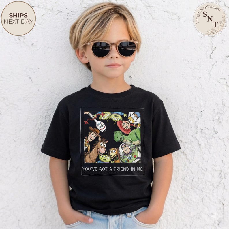 May include: Black t-shirt featuring a colorful graphic of characters from the animated movie "Toy Story." The graphic includes Woody, Buzz Lightyear, and other characters. The text "YOU'VE GOT A FRIEND IN ME" is printed below the graphic.