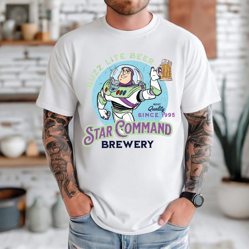 Puede incluir: Camiseta blanca con un dise&ntilde;o de dibujos animados de Buzz Lightyear sosteniendo una jarra de cerveza. El dise&ntilde;o incluye el texto "Buzz Lite Beer" y "Star Command Brewery" con "Best Quality Since 1995".
