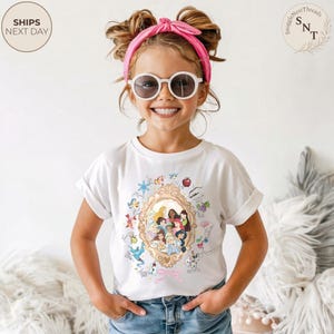 May include: A white t-shirt with a gold-framed portrait of Disney princesses and cartoon illustrations. The girl is wearing sunglasses and a pink headband. The shirt design includes characters like Cinderella, Snow White, and Belle.