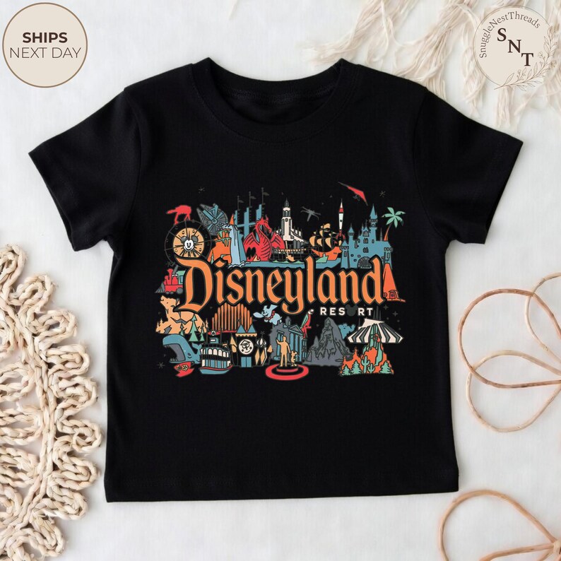 May include: Black t-shirt featuring a colorful graphic of Disneyland Resort. The design includes various park icons and the Disneyland logo in orange and red. The shirt is a classic crew neck style.