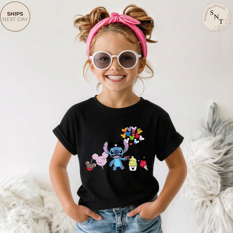 Pu&ograve; includere: T-shirt nero con una grafica colorata del personaggio Stitch che tiene in mano palloncini e coni gelato. Il design include zucchero filato rosa e palloncini a forma di Topolino. La maglietta &egrave; indossata da un bambino.