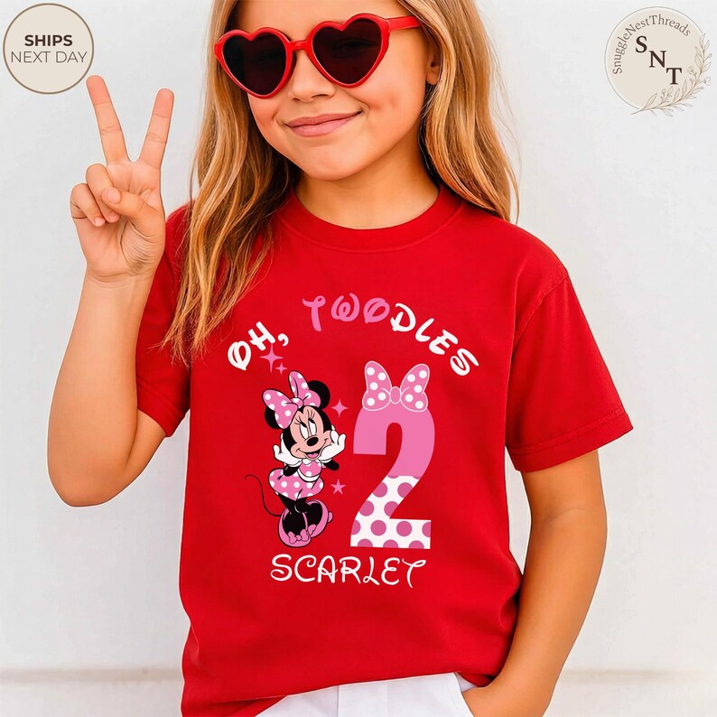 Puede incluir: Camiseta roja con un dise&ntilde;o de Minnie Mouse. La camiseta presenta el texto "Oh, Twoodles" y el n&uacute;mero "2" en rosa con lunares blancos. El nombre "Scarlet" est&aacute; impreso debajo.