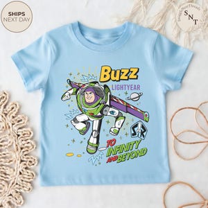 Puede incluir: Camiseta azul claro con un dise&ntilde;o de Buzz Lightyear de Toy Story. El dise&ntilde;o incluye el texto "Buzz Lightyear" y "To Infinity and Beyond". El personaje est&aacute; representado en su traje espacial verde y blanco.