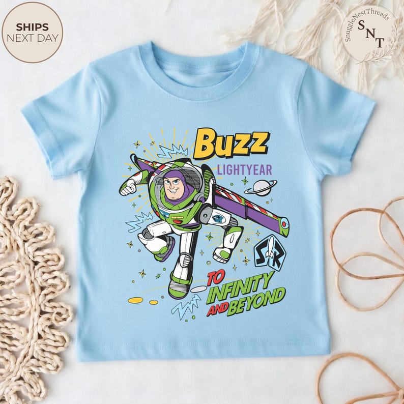 Puede incluir: Camiseta azul claro con un dise&ntilde;o de Buzz Lightyear de Toy Story. El dise&ntilde;o incluye el texto "Buzz Lightyear" y "To Infinity and Beyond". El personaje est&aacute; representado en su traje espacial verde y blanco.