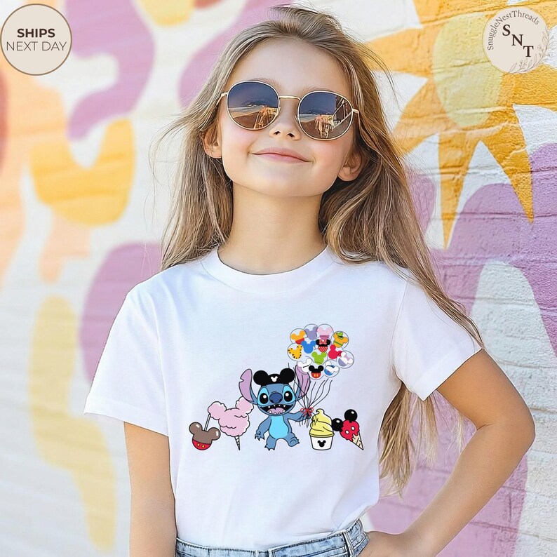 Pu&ograve; includere: T-shirt bianca con un personaggio dei cartoni animati che tiene in mano palloncini, zucchero filato e coni gelato. Il personaggio &egrave; blu con grandi occhi e orecchie nere. La maglietta &egrave; indossata da una persona con occhiali da sole.