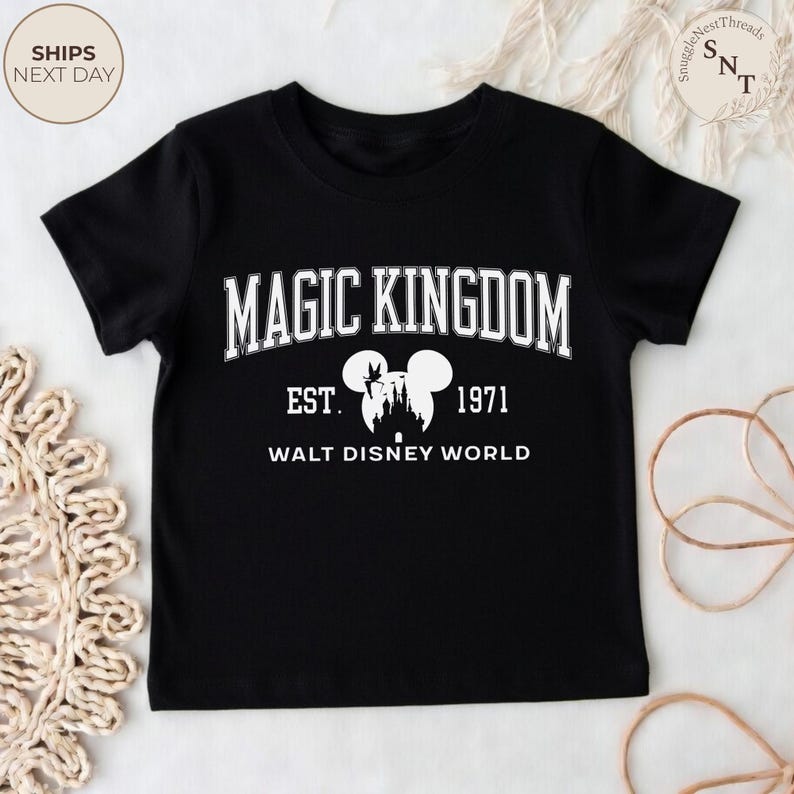 May include: Black t-shirt featuring the text "MAGIC KINGDOM" in white, with "EST. 1971" and "WALT DISNEY WORLD" below. A silhouette of the Disney castle and Mickey Mouse ears are also featured. A classic design for Disney fans.