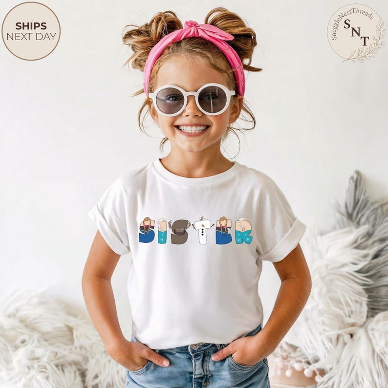 K&ouml;nnte beinhalten: Ein wei&szlig;es T-Shirt mit dem Wort "SISTER" auf der Vorderseite in bunten, cartoonartigen Buchstaben. Die Buchstaben zeigen Illustrationen von Figuren. Das Kind tr&auml;gt eine Sonnenbrille und ein rosa Stirnband.